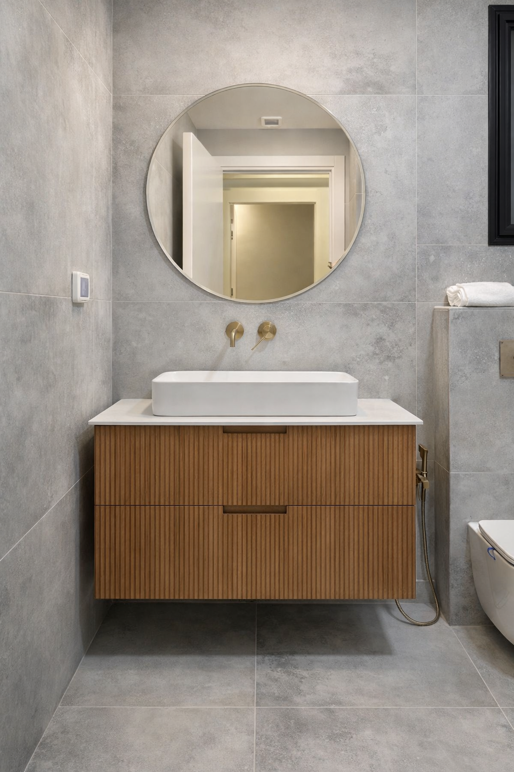 The bathroom: a fluted wood cabinet, a white sink, gold-tone faucets and a round mirror