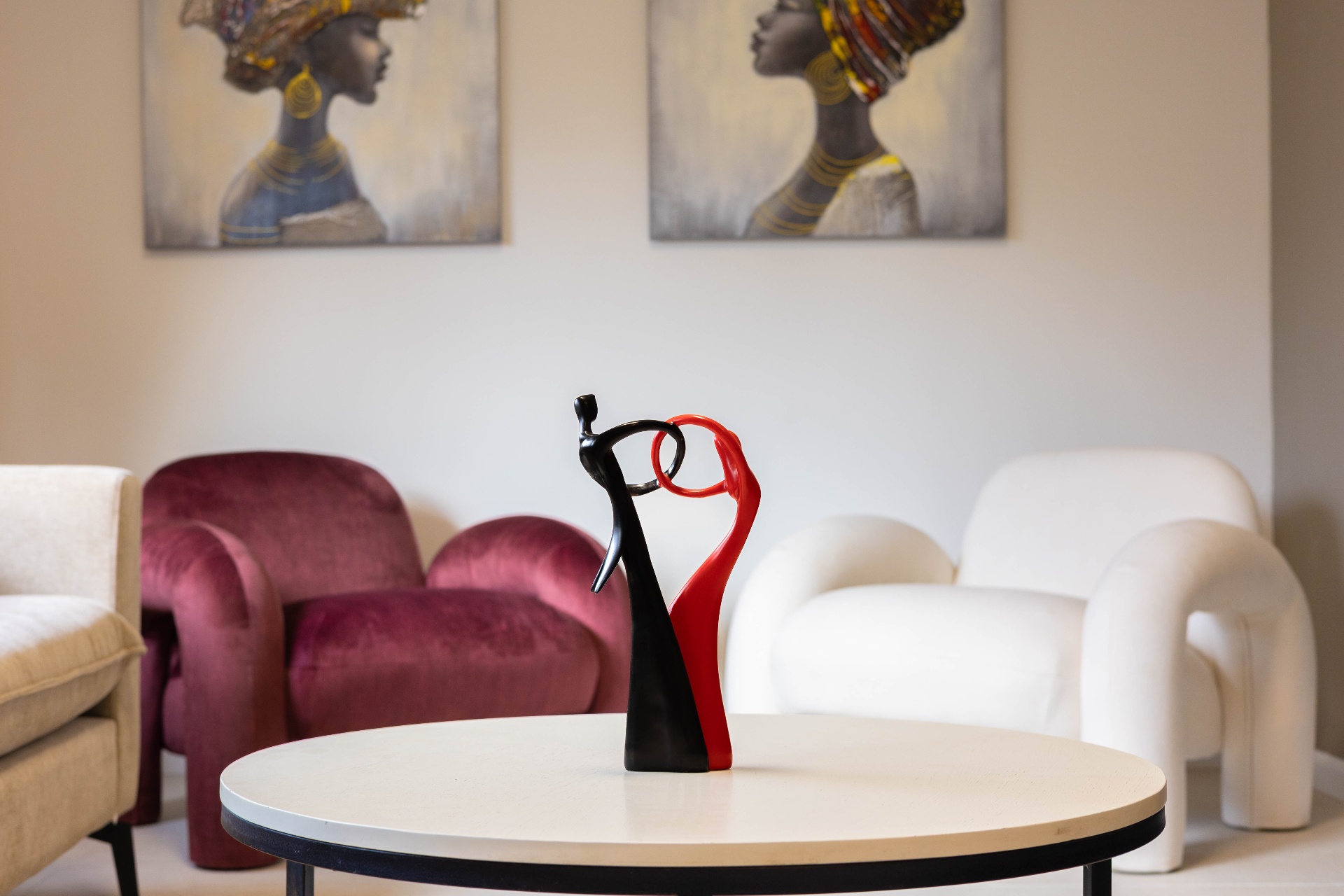 A red and black sculpture on the marble table, with the velvet armchair and the bouclé armchair behind it